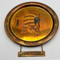 Front view of brass plaque showing pharaoh motif, ankh, rim design and attached inscription tag