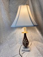 Full view of lamp lit showing marble base, ceramic body, shade