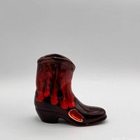 Right side view of glazed pottery boot showing red-orange drip over black and gold Brandon Canada script