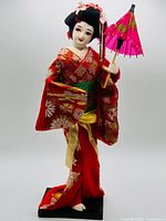 Front view of geisha doll showing kimono, parasol, face and base