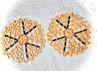 Two round bamboo woven trivets with orange and purple accents on white cloth backdrop