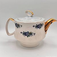 Right-side profile showing blue floral transfers, gold spout and handle, and overall crackle glaze