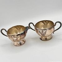 Front view of creamer and sugar bowl showing shape, handles, pedestal bases, tarnish