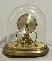 Front view showing complete clock with glass dome and brass base
