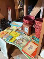 Books, red baskets, clock, cat vase, pouches displayed on shelving