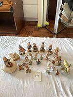 Group shot of approximately 23 Goebel Hummel porcelain figurines arranged on white cloth