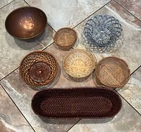 All seven serveware items laid out: copper bowl, metal basket, and five woven baskets including long oval bread basket