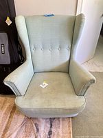 Front view of light green wingback armchair showing upholstery, button-tufted back, removable cushion and legs