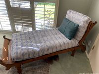 Side view of the chaise showing wood frame, patterned cushion and accent pillow