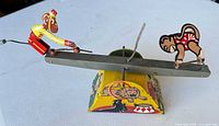 Full view of tin see-saw toy with two monkey figures on beam and decorated base