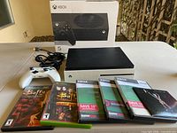 Console, controller, cables, five game cases and original box displayed on table