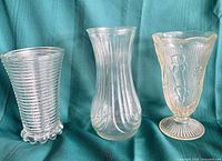 Three clear glass vases side by side on teal cloth