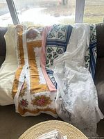 Five different tablecloths draped over sofa back showing colors and patterns