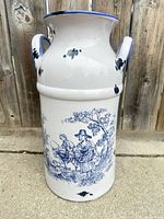 Front view of white ceramic milk can jug with blue pastoral scene and handles