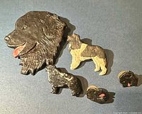 Overview of all five carved Newfoundland dog pins and brooches on blue surface