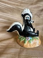 Front right view of glossy ceramic Flower the Skunk figurine on floral base