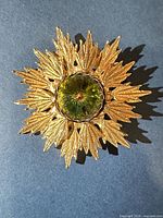 Front view showing gold-tone sunburst rays and green stone
