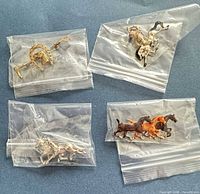 All four horse-themed brooches in zip bags