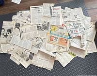 Pile of assorted loose 1980s newspaper pages and clippings spread on floor mat