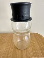 Front view of clear glass peanut-shaped jar with black top-hat lid