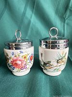 Front view of both egg coddlers showing floral and bird patterns with chrome lids