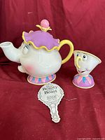 Mrs. Potts teapot, Chip teacup and hang tag on red backdrop