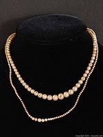 Both pearl necklaces displayed on black bust