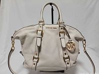 Front view of ivory leather Michael Kors Bedford Belted satchel showing handles, belted accents, MK charm