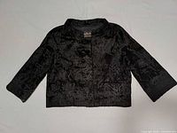 Full view of black broadtail fur cropped jacket laid flat