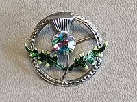 Front view of circular Mizpah Scottish thistle brooch showing enamel leaves and central rivoli rhinestone