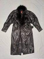 Full view of leather trench coat laid flat showing overall condition, length, belt and appliqués