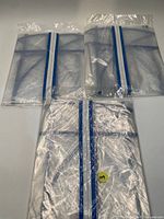 Three folded clear PVC suit bags showing blue trim and zipper