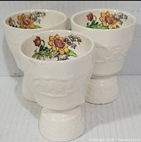 Front view of three cream double-sided egg cups showing floral interiors