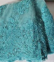 Folded turquoise sheer fabric showing embroidered edge with beads and sequins