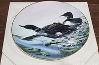 Front of round collector plate showing loon family artwork and gold rim