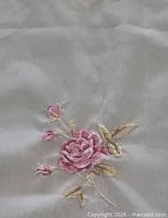 Close-up of embroidered pink rose and buds on white semi-sheer fabric