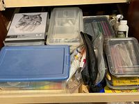 Drawer with multiple plastic bins, sketch pad, medium bottle, pencils and pens visible