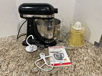 Overall view of KitchenAid mixer with bowl, three attachments, manual, and Oscar juicer