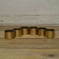 Six brass napkin rings front view on wood surface