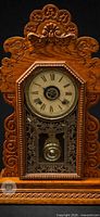 Front view of carved wooden Eastlake mantel clock showing dial, glass door, carvings and base