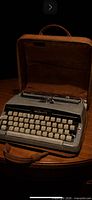 Typewriter seated in open carry case on table, keys and Majestic badge visible