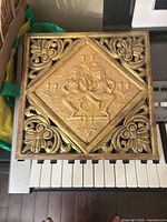 Front view of square carved gilt wood plaque on keyboard background