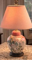 Front view of lamp showing painted bird and floral design, pink shade, wood base