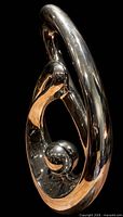 Three-quarter view of chrome abstract sculpture showing looping form and sphere