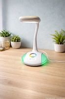 Front view of OttLite desk lamp on wooden surface, unlit head, green base glow visible