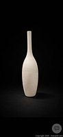 Full view of tall ribbed ivory ceramic vase against black background