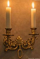 Single brass two-arm sconce mounted on wall with lit candles