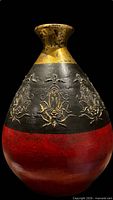 Front view showing bulbous shape, red base, black band with gold floral relief, gold neck