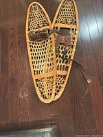 Pair of wooden snowshoes lying on floor showing rawhide lacing and leather bindings