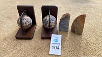 Two wooden globe bookends and two stone bookends displayed upright on carpet